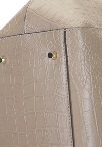 Sac à main en cuir beige avec embossage crocodile, vue de côté, présentant des accents en métal doré et des coutures robustes le long des coutures.