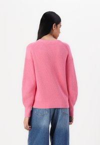 Rosa strikkegenser med ribbestruktur og ballongermer, kombinert med løst sittende blå denimjeans. Enkel rund hals design.