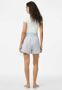 Šviesiai mėlynos languotos šortai su elastine juosta ir šoninėmis juostelėmis, derinami su prigludusia baltos spalvos marškinėliais. Lygios šlepetės puikiai užbaigia įvaizdį.