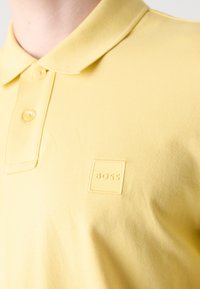 Gul polo skjorte laget av teksturert stoff, med krage, to-knapp placket og en preget logo lapp på brystet.