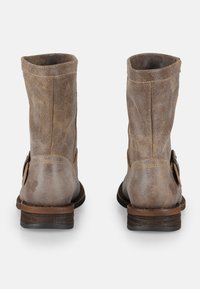 Botas de cuero marrón hasta el tobillo con una textura desgastada, caña recta y un sencillo detalle de hebilla en el lateral. Suela y tacón robustos en marrón.