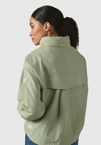 Light green jacket with a high collar, snap buttons, and a relaxed fit. Features a yoke design and small branded tag on the sleeve.