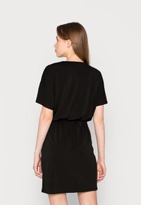 Vestido preto de manga curta com um corte descontraído, cintura franzida e textura suave. A bainha termina acima do joelho, oferecendo um design minimalista.