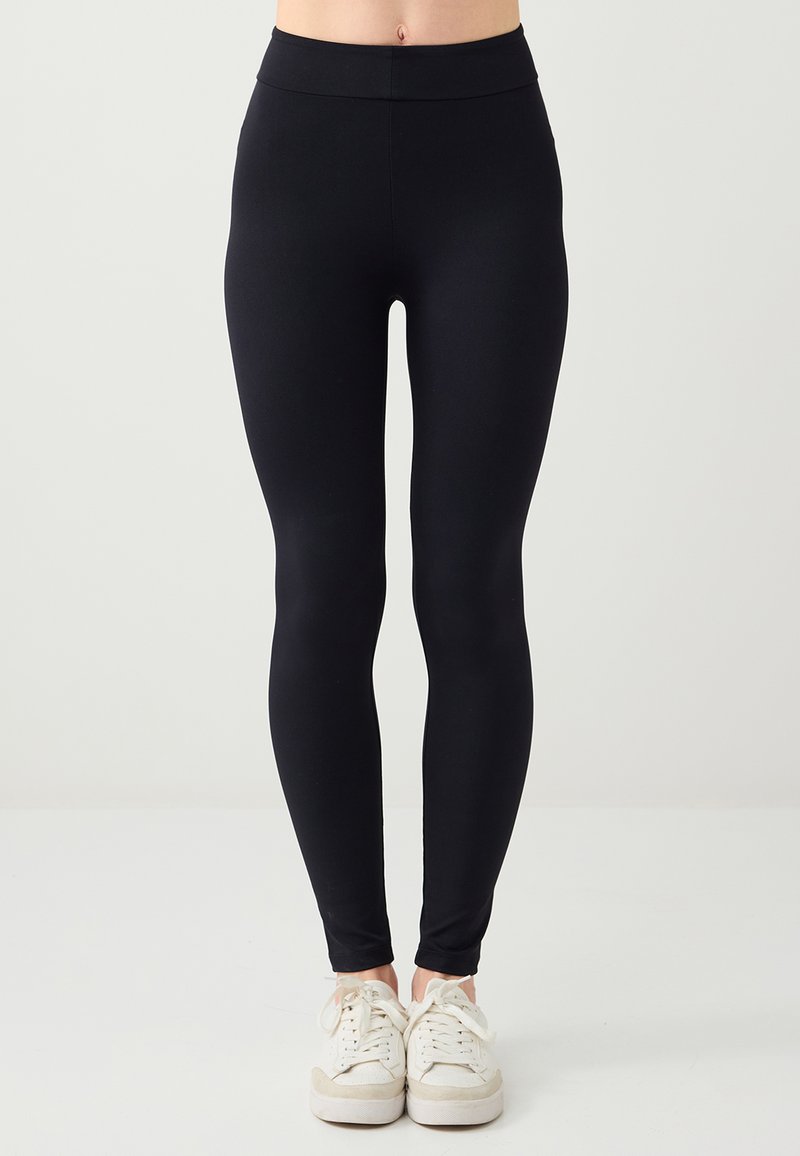 Legging noir fabriqué en tissu extensible avec une taille haute, une coupe ajustée, une texture lisse et sans motifs ni accents visibles.
