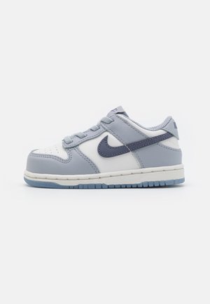 Αθλητικά παπούτσια Nike με πάνω μέρος από γκρι και άσπρο δέρμα, γκρι κορδόνια, ναυτικό λογότυπο Swoosh και διαφανή μπλε καουτσούκ σόλα. Σχεδίαση χαμηλού τύπου.