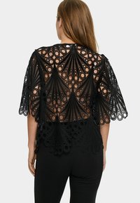 Top in pizzo nero con un motivo intricato e ritagli circolari, maniche corte e vestibilità ampia, abbinato a pantaloni neri attillati.