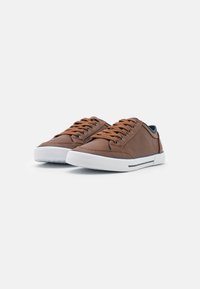 Baskets en cuir marron avec semelles en caoutchouc blanc, bout rond et accents bleu foncé contrastants. Comprend des œillets circulaires et des lacets marron.