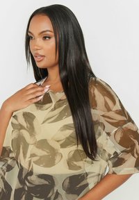 Top fluido e trasparente in beige con un motivo a foglia in tonalità di marrone. Presenta una vestibilità ampia e maniche larghe, il collo è rotondo e rilassato.