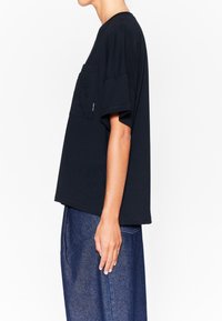 Camiseta de algodón negra con un corte holgado, mangas cortas y un bolsillo con bordado en la parte delantera. Tejido texturizado.