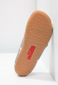Sneaker en tissu gris avec semelle en caoutchouc. Présente une texture en zigzag et un logo rouge sur la semelle extérieure. Taille indiquée comme 25.