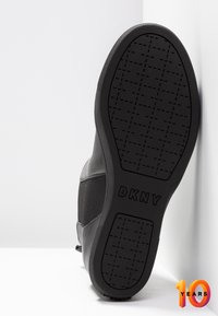 Zwarte sneaker met een textuur rubberen zool met DKNY-logo, glad leren en flexibel stoffen bovenwerk, ontworpen voor comfort en ondersteuning.