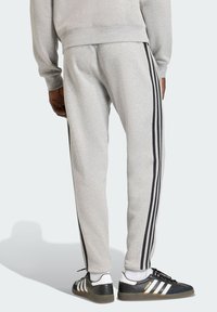 Sive trenirka hlače s crnim bočnim prugama, suženim nogavicama, elastičnim pojasom i mekim materijalom. Nošene s crno-bijelim tenisicama.