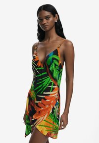 Vestido floral colorido con patrones vibrantes en verde, naranja y amarillo sobre un fondo negro; tirantes tipo espagueti con acentos de madera.