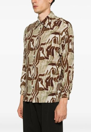 Uomo che indossa una camicia a maniche lunghe con motivo astratto marrone, beige e verde oliva, abbinata a pantaloni neri, in piedi di lato.