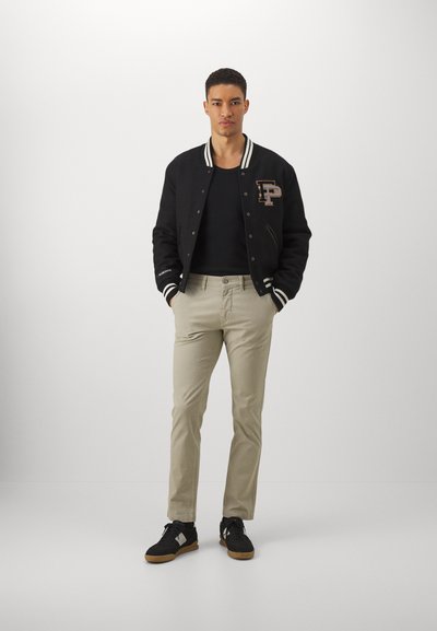 Black varsity jacket with striped cuffs, black tank top, beige slim-fit pants, and black sneakers with gum soles. Simple design and neutral colors.