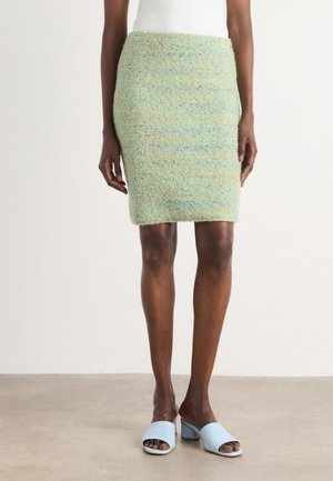 Lichtgroene tweed rok tot de knie met een gestructureerde afwerking. Gepaard met lichtblauwe open teen muiltjes. Eenvoudige top, zonder zichtbare details.