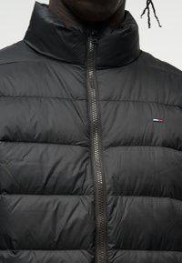 Black quilted jacket with high collar zipped up, showing small red, white, and blue logo on the left chest area.