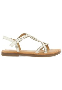 Sandalias planas blancas con un diseño entrecruzado y acentos metálicos, tiras ajustables en el tobillo y una suela texturizada marrón.