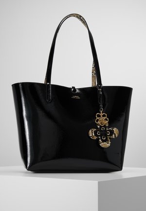 Błyszcząca czarna torba typu tote z uchwytami o wzorze skóry węża i dekoracyjnym kwiatowym breloczkiem wiszącym z przodu.