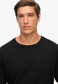 Sort crew-neck t-shirt lavet af bomuld, med et subtilt præget logo på brystet, glat tekstur og afslappet pasform.