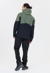 Vandtæt jakke med et grønt og marineblå design; har hætte, tofarvet stof og er parret med sorte bukser og mørke fodtøj.