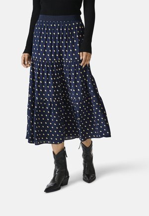 Personne portant une jupe midi bleu marine à pois beige, un haut noir à manches longues et des bottines noires à bout pointu.