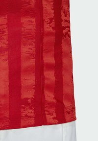 Camiseta deportiva roja con un patrón texturizado y rayas verticales, hecha de un tejido transpirable, que muestra un dobladillo suave y detalles de costura.