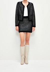 Svart och vit texturerad tweed-jacka och kjolset, med rund halsringning och mjuka manschetter, i kombination med beige knähöga stövlar.