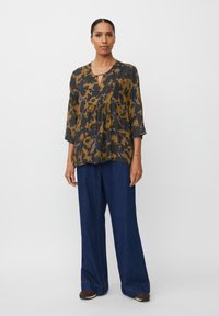 Bluse med sort og sennepsmønstret design, med nøglehul-udskæring, trekvartærmer og en afslappet pasform, parret med vidde bukser i mørk denim.