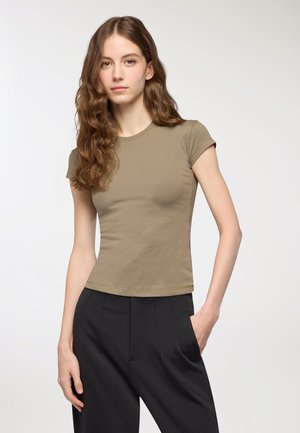 T-shirt fitted color verde oliva con maniche corte, texture liscia e scollatura rotonda classica, abbinato a pantaloni neri a vita alta.