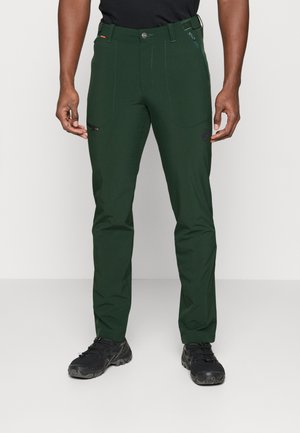 Green, slim-fit outdoor pants with multiple pockets, a zippered side pocket, and textured fabric, paired with black footwear.