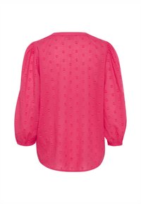 Blouse rose avec des manches ballon, encolure ronde et un motif texturé de cœurs en relief sur l'ensemble. Tissu doux, finition semi-transparente.
