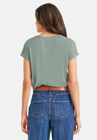 Korte mouwen, cropped t-shirt in saliegroen met een relaxte pasvorm. Gecombineerd met hoog getailleerde blauwe jeans met zichtbare achterzakken.