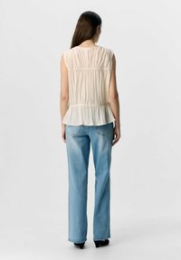 Haut sans manches beige clair avec texture froncée et taille peplum, associé à un jean droit bleu clair. Des talons noirs complètent la tenue.