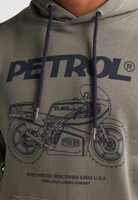 Sudadera de color verde oliva con un diseño gráfico en navy de una motocicleta, junto con el logo y el texto "PETROL" en la parte inferior. Los cordones son de color navy.