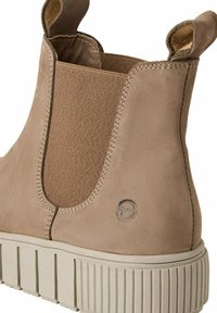 Bottines en cuir beige avec des panneaux latéraux élastiques, semelle texturée robuste et tirette au talon. Logo embossé subtil sur le côté extérieur.