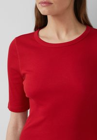 Rode geribbelde t-shirt met een ronde hals en korte mouwen. De stof lijkt glad met zichtbare textuurdetails langs de naden.