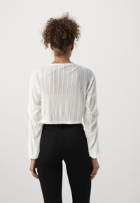 Pull blanc court avec texture à côtes verticales, manches longues et col rond, associé à un jean noir ajusté.