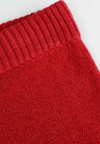 Czerwona dzianina z teksturowanym, prążkowanym mankietem i gładkim, jednolitym splotem. Materiał ma delikatny połysk.