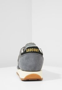 Gray suede sneaker with a black fabric heel tab featuring gold "SAUCONY" text, white midsole, and gum rubber outsole.