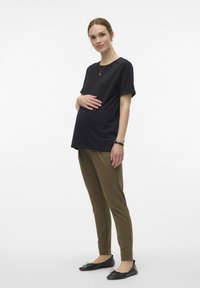 Top de maternidade preto de manga curta combinado com calças slim-fit verde-azeitona. O modelo usa sapatilhas pretas e um colar simples de ouro.