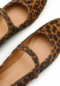 Bailarinas de estampado de leopardo con punta redonda, material de ante suave y tira en el tobillo, con una plantilla en un tono beige natural y acentos en negro.