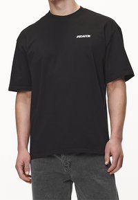 Camiseta de algodón negra con mangas cortas, cuello redondo y un logo blanco en el lado izquierdo del pecho. Textura suave y corte relajado.