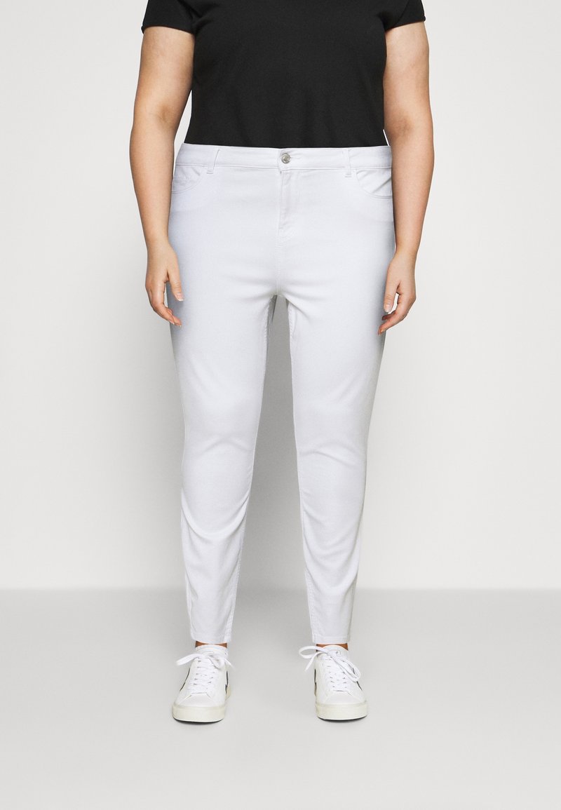 Pantalones ajustados blancos de mezcla de algodón, con cremallera frontal, bolsillos y una textura suave. Combinados con una blusa negra de manga corta.