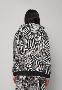Sudadera a rayas de cebra en blanco y negro con capucha ajustable, puños y cinturilla de canalé negra. Presenta un acabado de tela suave y texturizada.