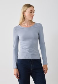 Light blue long-sleeve shirt with a round neckline, made of soft fabric, fitted design, paired with dark jeans. Simple and sleek.