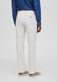 Witte broek met een slim fit, voorzien van achterzakken met knoopaccenten. Gedirigeerd met een blauwe jeanshemd en beige schoenen.