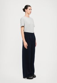 Camiseta de algodón gris de manga corta combinada con pantalones sueltos de color marino, con cintura alta y piernas anchas, completados con zapatos negros.