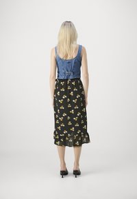 Farmernadrág stílusú cropped top állítható gombos záródással, fekete virágmintás midi ruhára rétegezve, amely fodros szegéllyel és apró sárga, valamint fehér virágokkal díszített.