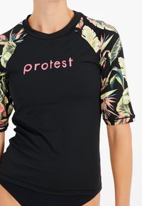 Musta rash guard lyhyillä hihoilla, jossa on värikäs kukkakuosi hihoissa. Etupuolella pinkki "Protest"-logo.